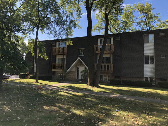 Front view of a multi-story apartment building with balconies and a gabled entrance.