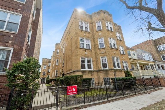 Front view of a multi-story brick apartment building with a 'For Rent' sign.