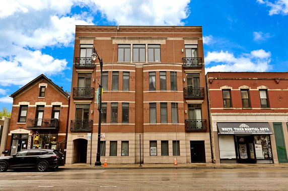 Front view of a multi-story brick building with large windows and small balconies.