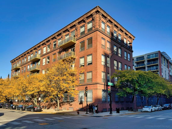 Front view of a multi-story brick building with balconies on a street corner.