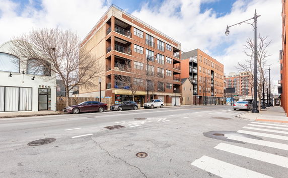 Front view of a multi-story brick residential building with balconies and adjacent structures.