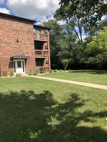 Front view of a multi-story brick building with balconies and a walkway leading to the entrance.
