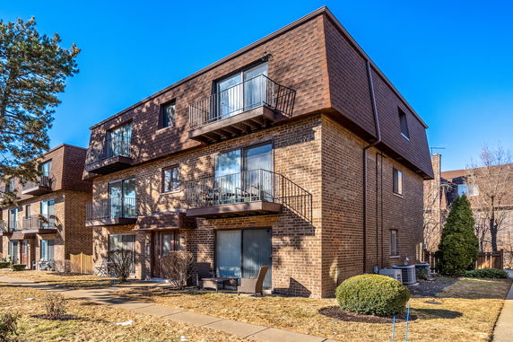 Front view of a three-story brick apartment building with balconies.
