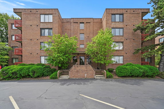 Front view of a multi-story brick building with large windows and greenery on both sides.