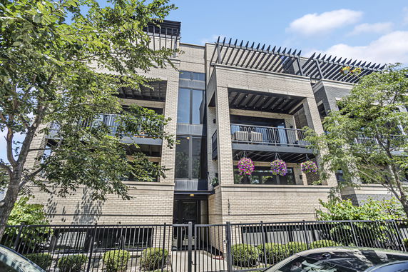 Front view of a multi-story brick apartment building with balconies and floral decorations.