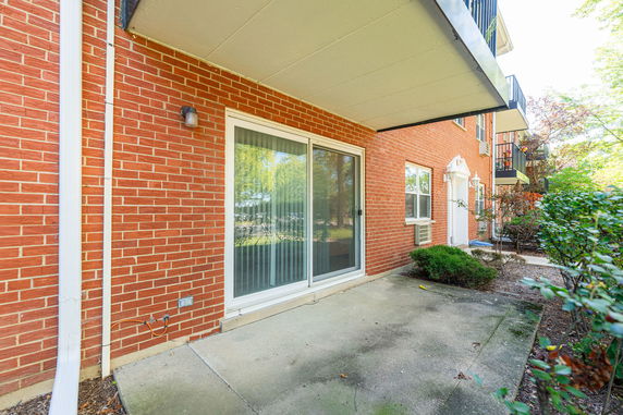View of a brick building's exterior with a sliding glass door and a small concrete patio.
