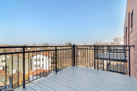 View from a balcony looking out over residential rooftops and distant cityscape.