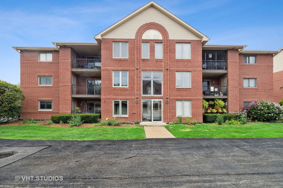 Front view of a three-story brick apartment building with balconies and windows.