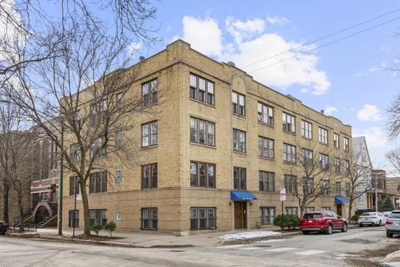 Front view of a multi-story brick apartment building with blue awnings over the entrances.