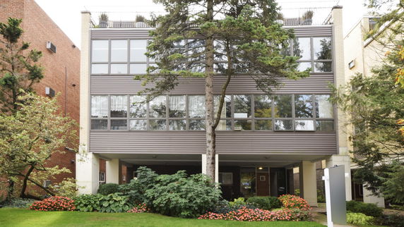 Front view of a multi-story building with large windows and a garden area in front.