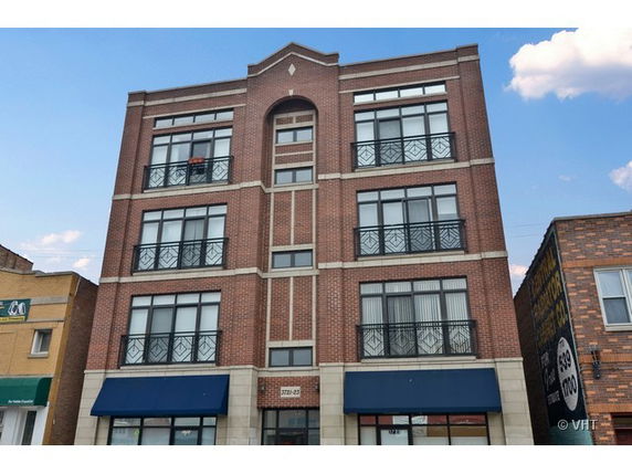 Front view of a four-story brick building with large windows and decorative railings.