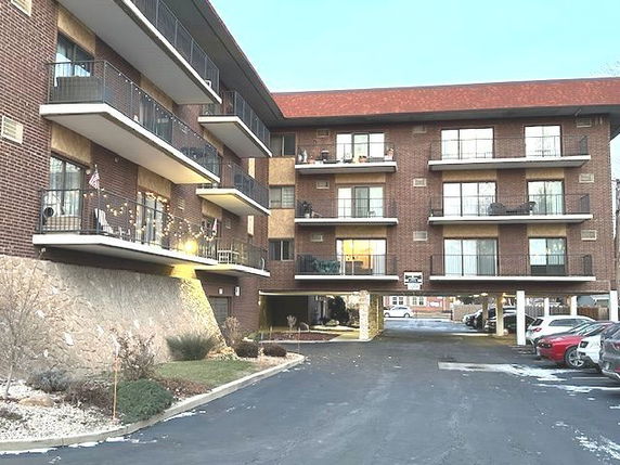 Front view of a multi-story residential building with balconies and parking area.