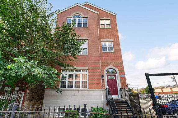 Front view of a three-story red brick building with a staircase leading to a red front door.