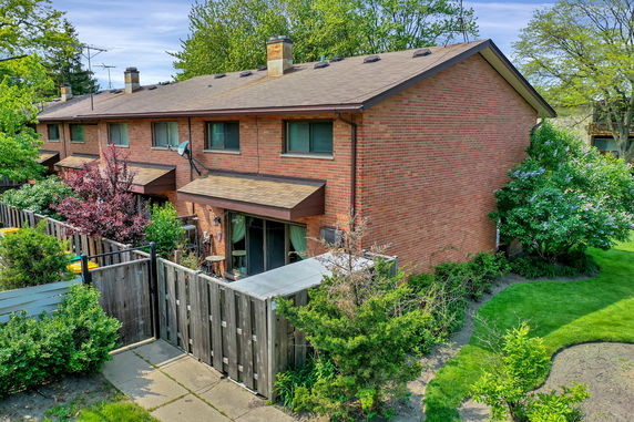 Side view of a two-story brick townhouse with fenced backyard and patio area.