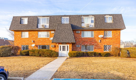 Front view of a multi-story brick building with a dark shingled roof and multiple windows.