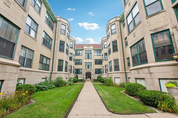 Front view of a multi-story brick apartment building with green window frames and an arched entrance.