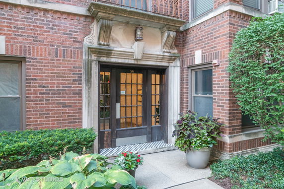 Front view of a brick building entrance with decorative stonework and plants.