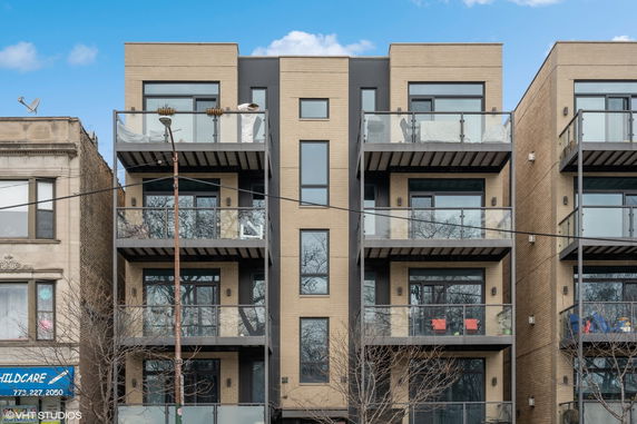 Front view of a modern multi-story apartment building with glass balconies.