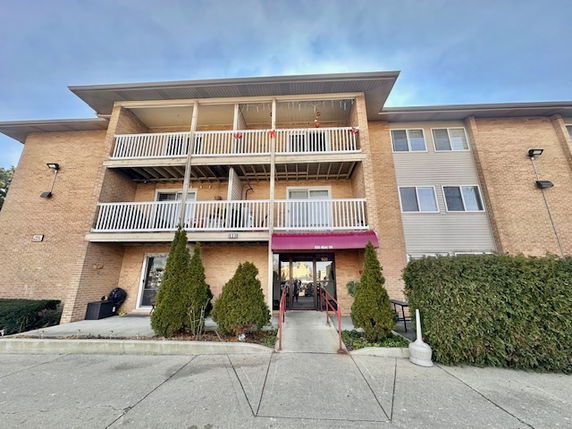 Front view of a three-story apartment building with balconies and a small entrance canopy.