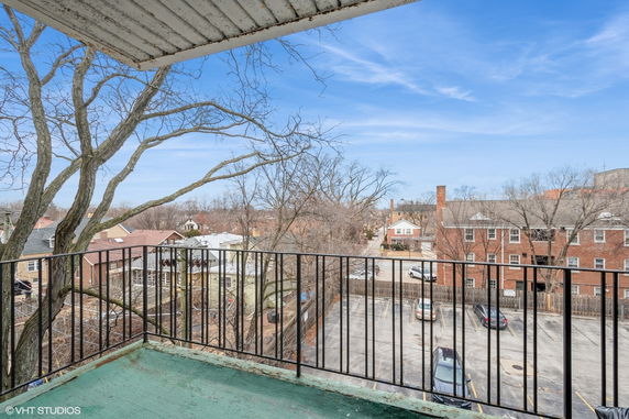 View from a balcony overlooking surrounding residential area with trees and parked cars.