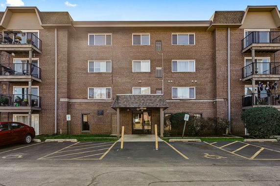 Front view of a four-story brick apartment building with a central entrance and balconies on both sides.