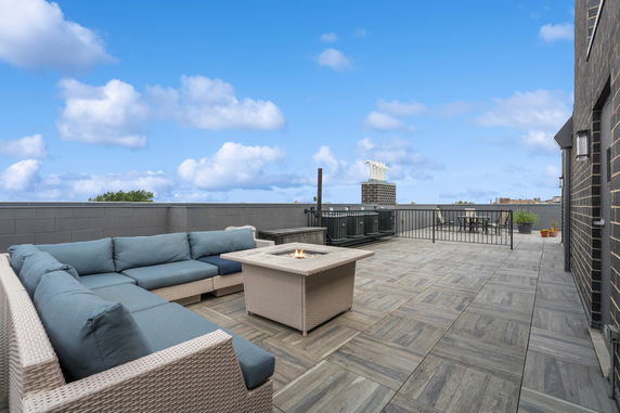 Rooftop with seating area and fire pit, featuring a tiled floor and clear blue sky.