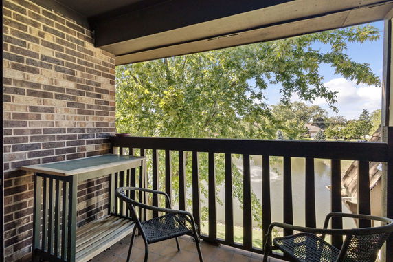 Balcony view with chairs overlooking trees and a pond.