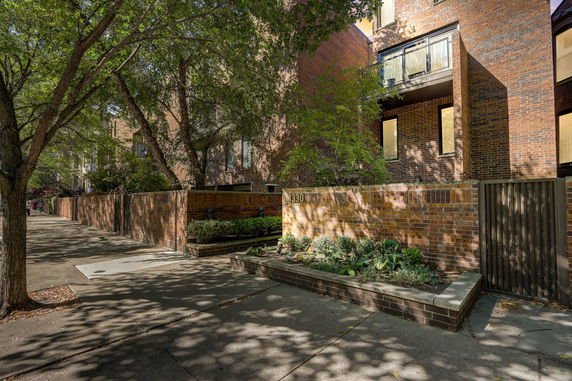 Front view of a brick building with balconies and plants along the sidewalk.