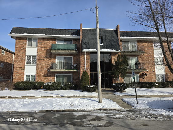 Front view of a three-story brick apartment building with balconies.