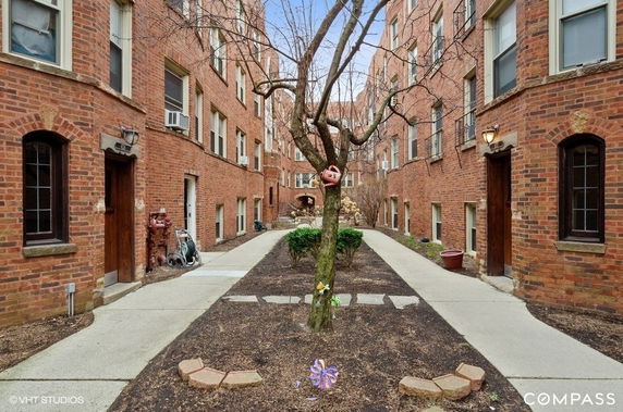 Front view of a brick apartment building with a tree and pathway in the courtyard.