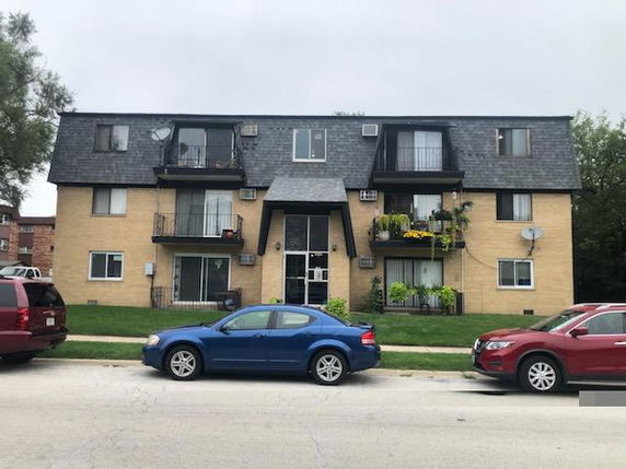 Front view of a multi-story apartment building with balconies and a shingled roof.
