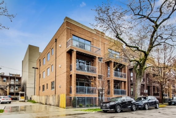 Front view of a multi-story brick building with balconies and a tree-lined street.