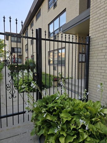 Front view of a multi-story building with a gated entrance and plants.