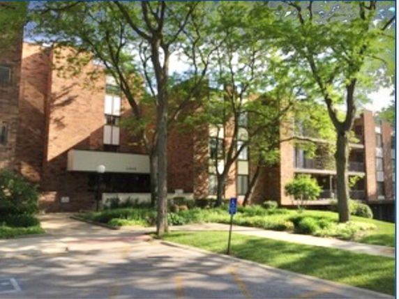 Front view of a brick apartment building with multiple stories and large trees in the foreground.