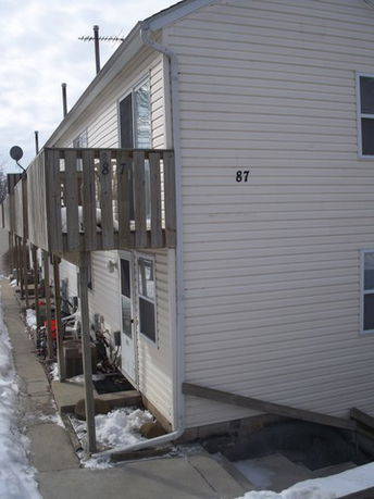 Side view of a two-story house with wood siding and an upper balcony.