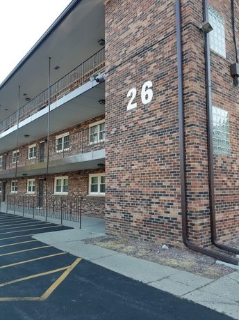 Front view of a multi-story brick building with metal railings and large number 26 on the facade.