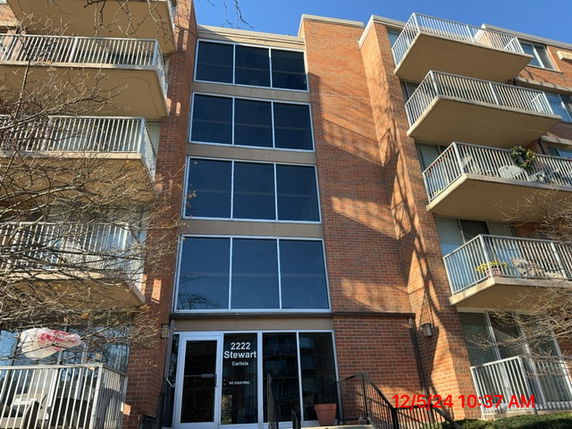 Front view of a multi-story brick apartment building with glass windows and balconies.