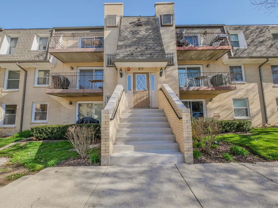 Front view of a multi-story residential building with balconies and a central entrance staircase.