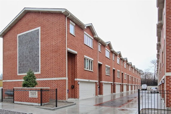 Front view of a row of three-story brick townhouses with garages.