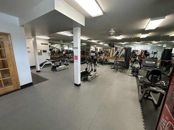 Indoor gym area with various exercise equipment and mirrors on the walls.