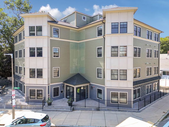 Front view of a multi-story residential building with multiple windows and a fenced entrance.
