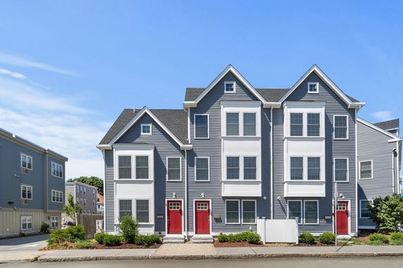 Front view of a multi-story townhouse with gabled roofs and red doors.