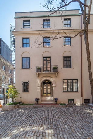 Front view of a multi-story building with arched windows and a cobblestone driveway.
