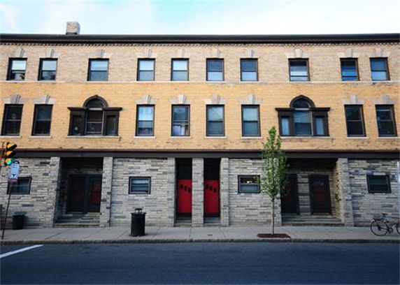 Front view of a three-story brick building with red doors and multiple windows.