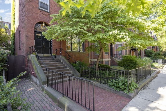 Front view of a traditional brick townhouse with a black door and stairs leading up to the entrance.