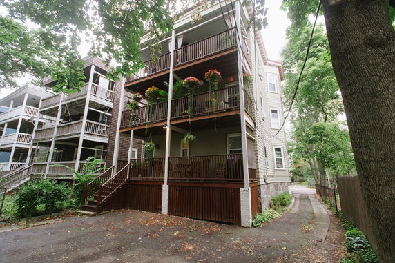 Front view of a multi-story residential building with wooden balconies and greenery.