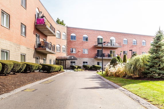 Front view of a multi-story brick building with balconies and a driveway leading to the entrance.
