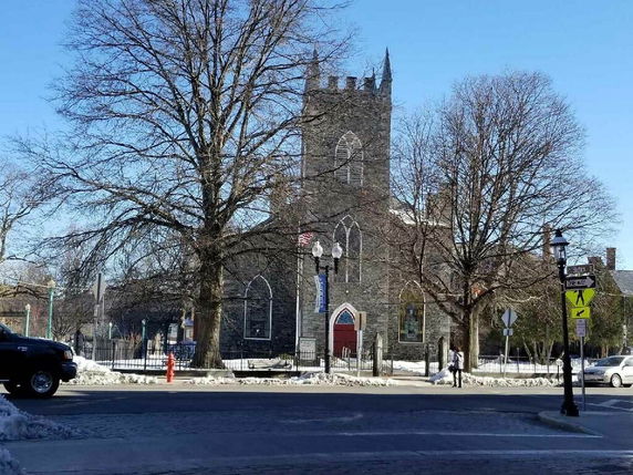 Front view of a stone church with a tower and arched windows.