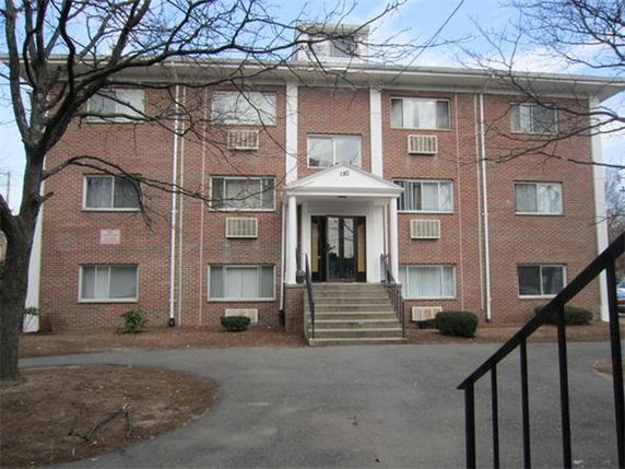 Front view of a three-story brick apartment building with steps leading to the entrance.