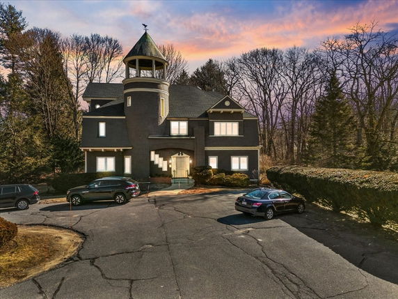 Front view of a house with a tower and multiple gables, surrounded by trees.